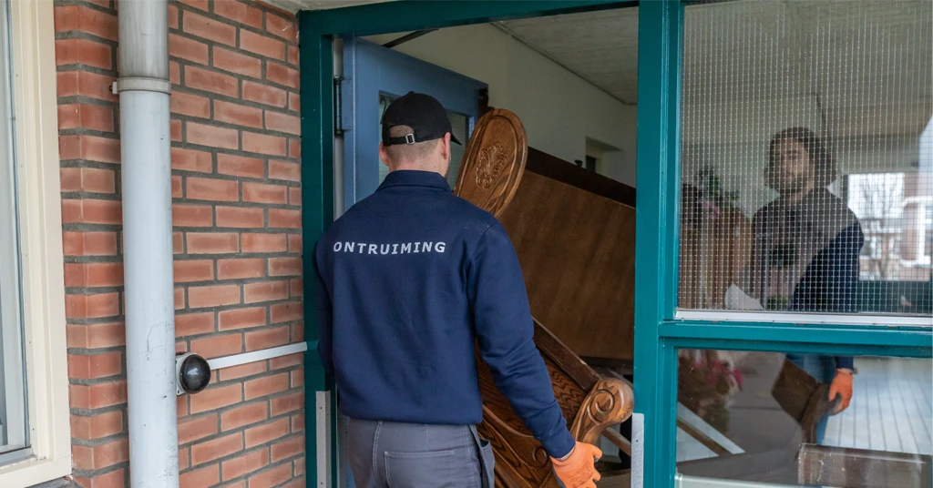 Twee medewerkers tillen samen spullen uit een huis